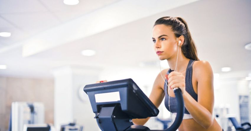 Machine Learning In Healthcare - Serious fit woman in earphones and activewear listening to music and running on treadmill in light contemporary sports center