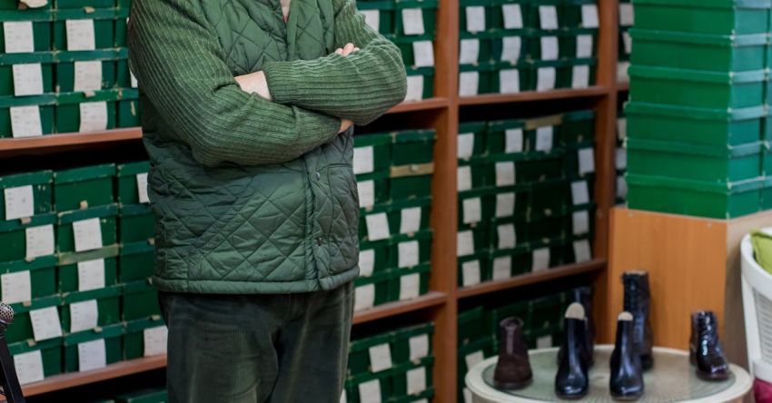Product Owner - Full body of calm ethnic male customer in uniform standing with crossed arms in shoe store against shelves with boxes and looking at camera